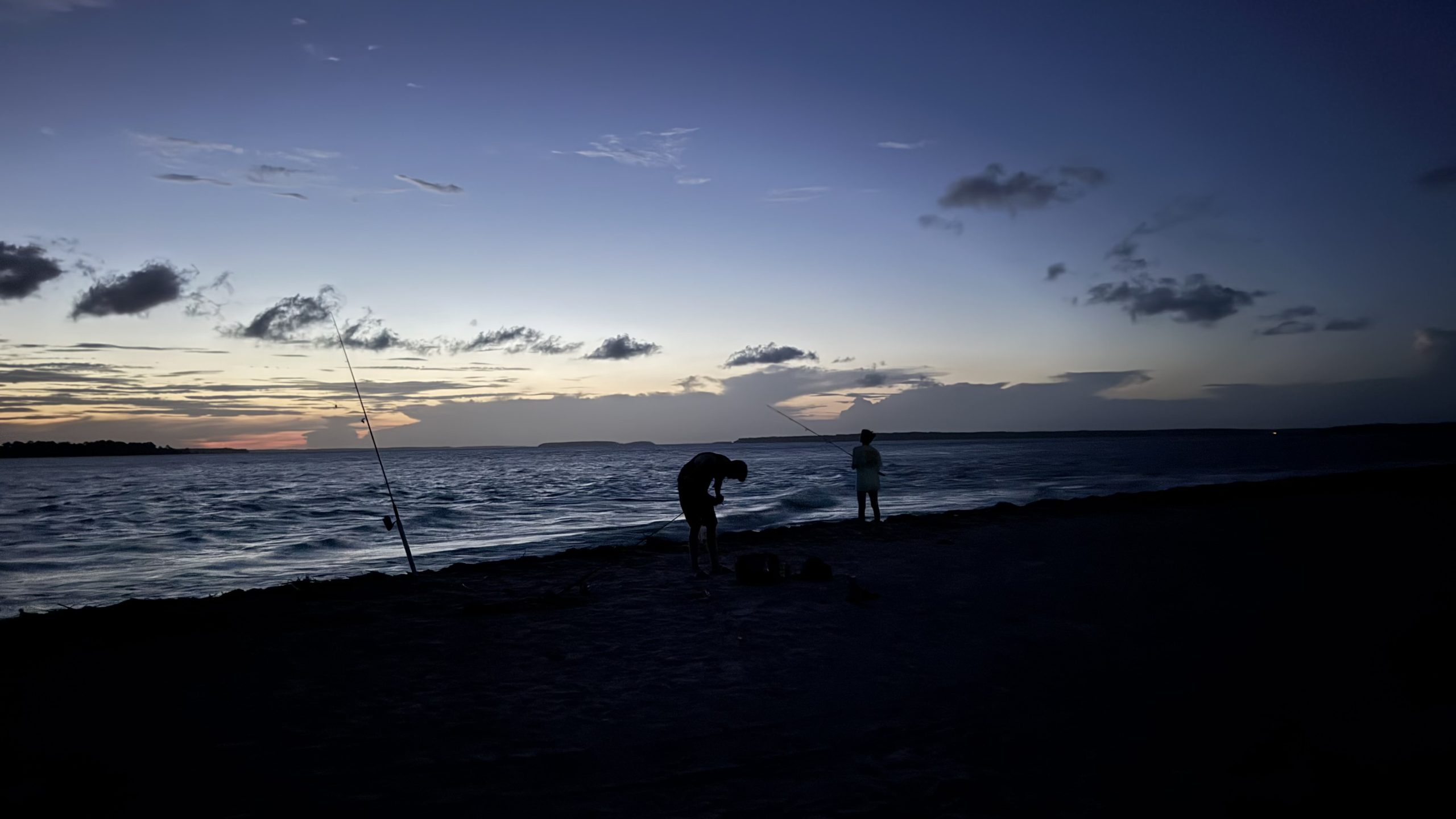 People fishing along the shoreline at dusk.